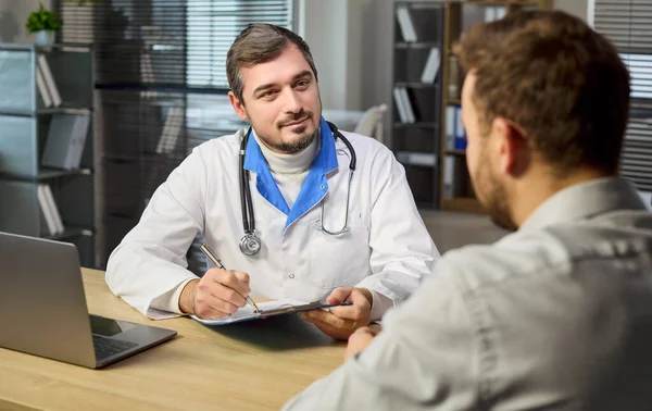 Klinikteki doktor ve hasta danışmanlığı. Steteskoplu bir doktor, not defterine not yazıp dinleyerek rutin kontrol sırasında empati ile tavsiye veriyor. Sağlık hizmetleri güven ve destek kavramı.