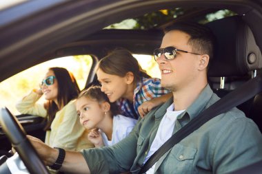 Yaz gezisinde mutlu aile arabaları, hafta sonları gülümseyen ebeveynler ve çocukların seyahat maceraları. Genç gülümseyen baba direksiyonu tutuyor, anne, oğul ve kız oturuyor ve ileriye bakıyor.