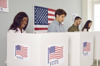 Demokratik başkanlık seçimlerinde oy kullanan çok ırklı Amerikan vatandaşlarından oluşan mutlu bir grup. ABD bayraklarıyla kabinlerde dikilen ve oy pusulalarında oy kullanan çok sayıda insan
