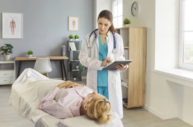 Hastanede kanepede uzanmış genç bir hasta muayene sırasında kendine güvenen bir kadın doktorla konuşuyor. Hastaların şikayetlerini dinleyen bir tıp çalışanı. Sağlık hizmetleri kavramı.