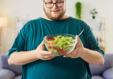 Gülümseyen adam evde salata kasesi tutuyor. Cam bir kasede kıtır kıtır marul ve sebzelere bakıyor ve sağlıklı beslenme niyetleri olduğunu söylüyor. Konsept: dikkatli yeme, sağlıklı yaşam tarzı alışkanlıkları.