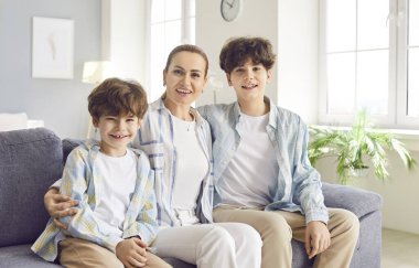 Evde iki oğlu olan mutlu ve gülümseyen bir annenin portresi. Aile bağlarının anne sevgisi ve sevinci, bir ebeveyn, ergen ve okul çocuğu oğulları arasındaki özel ilişkiyi vurguluyor..