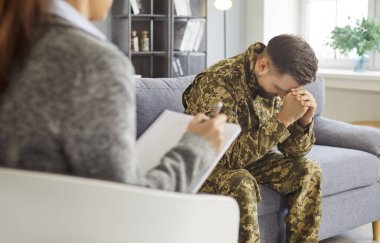 Genç gaziyle konuşan kadın psikolog, asker duygularla boğulmuş görünüyor, savaş sonrası stres bozukluğu ve diğer zorluklarla başa çıkıyor, klinikte profesyonel psikolojik destek alıyor