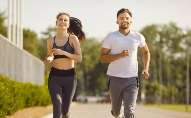 Yaz parkında koşan çiftlerin sağlıklı koşuşları, mutlu insanların gülümseyerek birlikte koşuşları. Spor giyim eğitiminde aktif formda bir kadın ve erkek, gülümsüyor. Coşkuyla antrenman, maraton konsepti