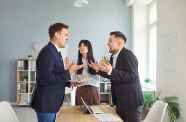 Bir ofiste, bir meslektaşı anlaşmazlığı çözmek ve anlaşmazlığı azaltmak için arabuluculuk ve pazarlığa başkanlık ederken, iki iş arkadaşı bir masada tartışıyor. İki iş arkadaşı arabulucu olarak tartıştı.