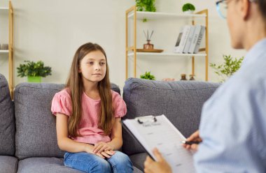 Çocuk psikoloğu kız için danışmanlık terapisi sunuyor. Genç hasta bir kanepede otururken danışman sakin bir seans ve güven içinde notlar alıyor. Çocuk sağlığı destek teması.