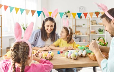 Mutlu, gülümseyen dört kişilik bir ailenin portresi. Komik tavşan kulakları takıp birlikte yumurta boyuyorlar. Evdeki mutfaktaki masada oturuyorlar. Anne, baba ve iki çocuk Paskalya bayramı kutlaması için hazırlanıyor..