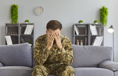 Kamuflaj üniforması giymiş bir erkek asker koltukta tek başına oturuyor, duygularla boğuşuyor, travma sonrası stres bozukluğu, travma, endişe veya depresyonla başa çıkıyor. Ruh sağlığı sorunları