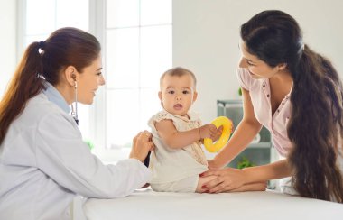 Muayene sırasında bebeği olan bir çocuk doktoru ve anne. Klinikte aile doktoru, bebek muayene masasında oturup oyuncaklarla oynarken steteskop kullanır. Pediatrik sağlık ve tıp.