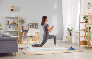 Aktif kadın atlet spor salonunda spor egzersizleri yapıyor, fitness 'e olan bağlılığını gösteriyor. Odaklanmış ifadesi ve şekli atletizmini ve egzersiz rutinine bağlılığını vurguluyor..