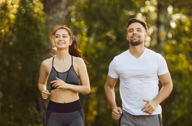 Aktif koşucu çiftlerin sabah koşusu, gülümseyen insanların yaz parkında koşu maratonu yapmaları. Spor giyim sektöründe kadın ve erkeğin dayanıklılık ve dayanıklılık eğitimi. Spor meydan okuma kavramı