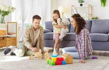 Ebeveynleri ve çocukları olan aile evde eğitici bir oyun oynuyor. Oturma odasında, ahşap evler yapıyorlar ve oyuncakları aşkla birlikte yere yığıyorlar. Aile oyunu, eğlence ve öğrenim.