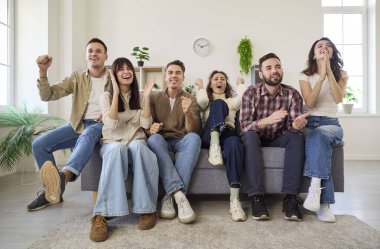 Arkadaşlar televizyonda futbol oynuyorlar. Yedi arkadaş bir kanepede oturur, parlak bir oturma odasında gergin bir maç izlerken el çırpar ve yumruk sallarlar. Neşeli ev sporu izleme partisi.