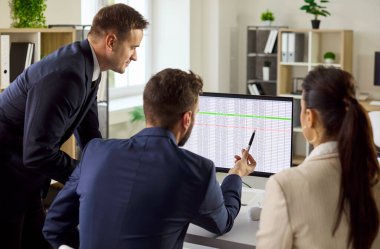 Ofisteki iş ekibi analiz veri stratejisinde. Meslektaşlar bir bilgisayar monitöründeki çizelgeleri gözden geçirir, planlama koordinasyonunu sağlar ve toplantı sırasında görevleri düzenlerler. Takım çalışması ve tartışma kavramı.