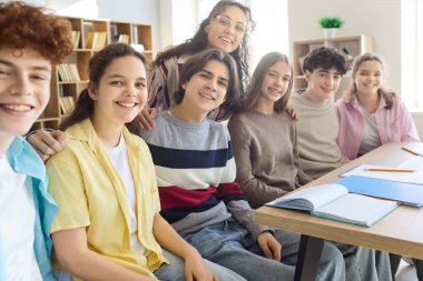 Öğrenciler ve öğretmenler sınıfta takım çalışması gösteriyor. Gülümseyen gençler birlikte bir masada dizüstü bilgisayarları ve defterleri ile birlikte otururlar, işbirlikçi öğrenme ve projelere hazırdırlar. Eğitim ve takım çalışması kavramı.