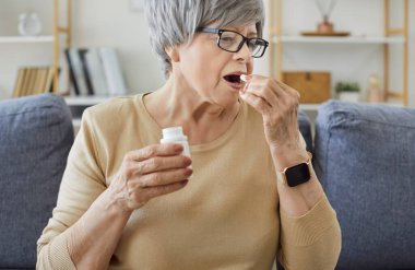 Son sınıf öğrencisi kadın hastalık tedavisi için hap alıyor, evdeki kanepede oturuyor. Günlük reçeteli ilaç, vitamin takviyesi ya da antibiyotik almak için elinde ilaç şişesi tutan yaşlı kişi