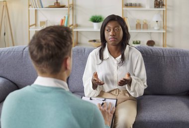 Genç üzgün Afrikalı Amerikalı kadın hasta psikolog ya da psikoterapist ile terapi seansı yapıyor, koltukta oturuyor, depresyonu, hayatı, işi ve ilişki sorunları hakkında konuşuyor.
