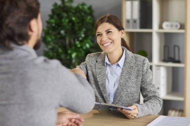 İş yerindeki acemi ve adayın iş görüşmesinde tokalaştık. Gülümseyen genç kadın ve erkek tokalaşıyor, profesyonel İK çalışanı pano tutuyor, iş arayanı karşılıyor ve özgeçmişi tartışıyoruz.