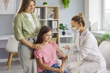 Klinikteki doktorun aşısı, gülümseyen çocuk. Hemşire şırınga ile enjeksiyon yapar. Annesinin sakin bir ofiste bakımı sırasında desteklediği gibi. Güvenlik, güven ve dokunulmazlığı vurgula.