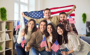 Gülümseyen arkadaşlar grubu bağımsızlık günümüzü kutluyor. Mutlu insanlar içeride vatansever ruhlarını paylaşarak Amerikan bayrağını sallıyor. Günlük kıyafetler ve parlak bir oda. Kavram: Ulusal gurur ve kutlama.