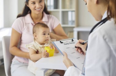 Çocuk doktoru danışmak için anne ve bebekle tanışır. Çocuk hasta klinikte oyuncaklarla oynarken aile doktoru panodaki terapi listesini inceliyor. Pediyatrik güven, bakım ve ilaç.