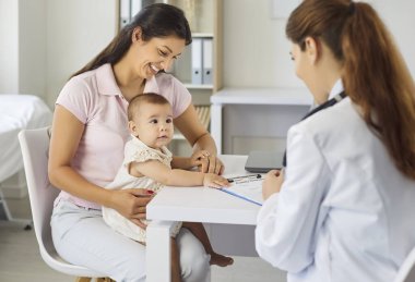 Anne ve bebek check-up için çocuk doktoruyla tanışıyor. Tıp kliniğinde aile doktoru, annemle büyüme, aşı ve gelişim konularını konuşur. Çocuk sağlığı, bakım, ilaç ve desteği kavramı.