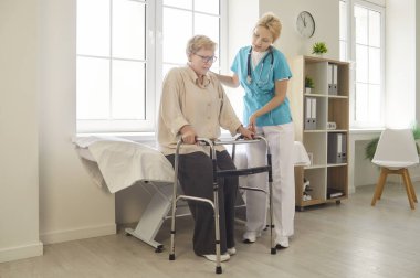 Klinikteki muayene masasından kalkmak için Walker 'ı kullanan yaşlı bir kadına yardım ve bakım. Engelli, fizyoterapi ve bakıcıdan yardım alan yaşlı hastalar için hastane taşınabilirlik yardımı