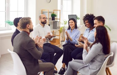 Genç neşeli iş adamları ofiste çember oluşturup toplantı odasında iş projesinden bahsedip alkışlıyorlar. Şirket çalışanlarının modern ofiste iş eğitimi var..