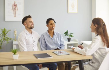 Gülümseyen genç çift kocası ve karısı masada oturup klinikte ya da hastanede hamilelik planlamada aile doktoru terapistiyle konuşuyorlar. Sağlık ve Tıp Konsepti.