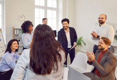 Mutlu gülümseyen şirket çalışanları modern ofiste el sıkışıyorlar. İş adamları, iş arkadaşlarıyla başarılı bir ortaklıktan memnuniyet duyuyorlar ve kapalı bir toplantıda onları alkışlıyorlar..