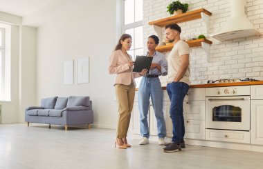 Genç evli çift, kadın emlakçıyla sözleşmeyi tartışıyor. Yeni evin mutfağında duran belgelere bakıyor. Aile ev sahibi olmaya hazır. Emlak piyasası kavramı.
