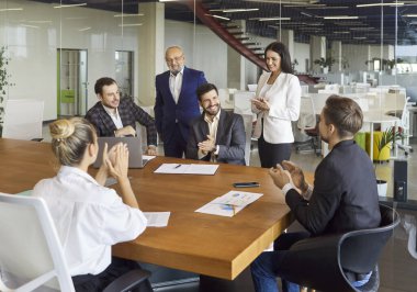 Şirket sözleşmesi imzalanırken iş ortaklarının alkışı. İnsanlar anlaşmayı ve ortaklığı onaylıyor, girişimciler masaya oturup kağıt imzalamak için duruyorlar