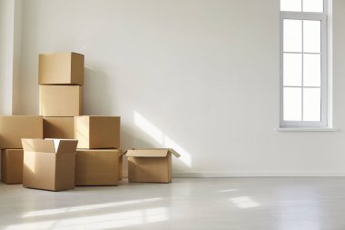 Geniş pencerenin yakınındaki boş güneş ışığı odasındaki karton kutular ev taşıma, teslimat ya da taşınma servisini işaret ediyor. Metin için doğal ışık ve boşluk içeren temiz, minimal iç mekan.