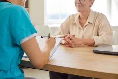 Hastanede hemşire ya da doktorla birlikte yaşlı kadın hastaya tıbbi danışma. Sağlık uzmanı, yaşlı bir kadınla dostane bir sohbette panoya teşhisle ilgili notlar yazıyor.