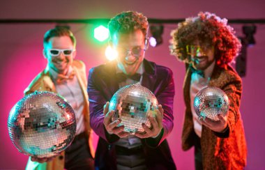 Disko dansçıları kostümlü adamlar. Müzik ve ışıklar, arkadaşların ayna topları ve neon ışıklarıyla eğlenceli enerjilerini paylaştıkları canlı bir kutlamaya yol açıyor. Eğlence için gece hayatı konsepti.