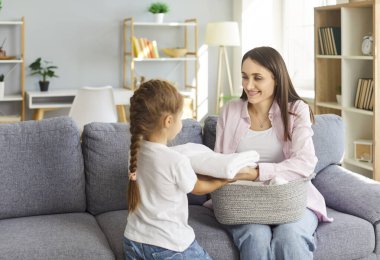 Neşeli küçük kız, gülümseyen annesine çamaşırhaneden sonra temiz havlu katlamasına yardım ediyor. Mutlu aile birlikte iyi vakit geçirir, ev işleri yapar ve çocuklara sorumluluk öğretir..