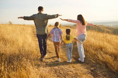 Mutlu aile tasasız yürür kollarını açarak altın saatin doğasında, arka planda. Ebeveynler ve çocuklar dengede, kollarını açarak manzaralı altın çayır yolunda, özgürlük ve birlikteliği gösteriyorlar, sevgi bağı kuruyorlar.