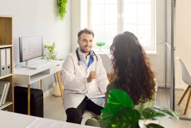 Klinikteki hastaya doktor muayenesi. Gülümseyen doktor randevu sırasında tavsiye ve tedavi sunuyor, notları gözden geçiriyor. Destekleyici ses tonu. Güvenilir sağlık hizmetleri iletişimi kavramı.