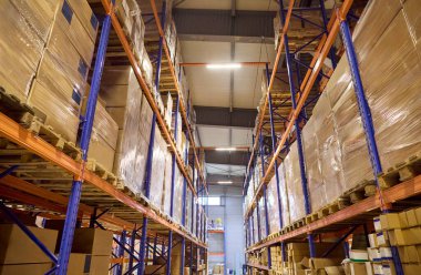 Paletler ve kutularla dolu bir depo rafı. Uzun raflar ve bir koridor gösterisi organize edilmiş envanter ve depo. Paketleme dağıtılmaya hazır olduğunu gösteriyor. Bugün depo verimliliği kavramı açık.