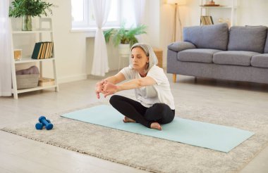 Yaşlı kadın evde esneme egzersizleri ve pilates yapıyor, spor ve sağlığa zaman ayırıyor. Spor rutini bir spor alanında esnekliği ve aktif bir yaşam tarzını vurgular.