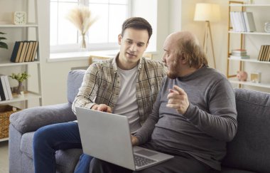 Yetişkin oğlu olgun babasına laptopun nasıl kullanılacağını öğretiyor, bir şeyleri açıklıyor ve koltukta birlikte poz verirken tavsiyelerde bulunuyor. İki nesil ve modern teknolojiler