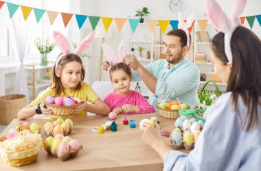Mutlu Paskalya aile dekorasyonları, bahar tatili geleneğinde yumurta renginde süslemeler, tavşanlı tavşan kulağı takan çocuklarla anne ve baba aktiviteleri, tatil partisi dekorasyonu, festival