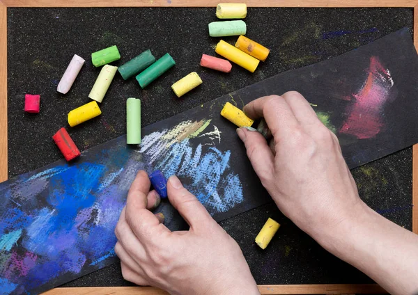 artist\'s hands with colored pastel crayons on a black background