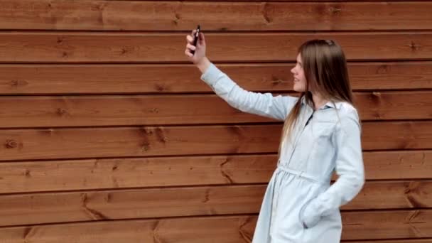 Feliz caucásico adolescente chica tomando un selfie en su teléfono de madera fondo — Vídeos de Stock