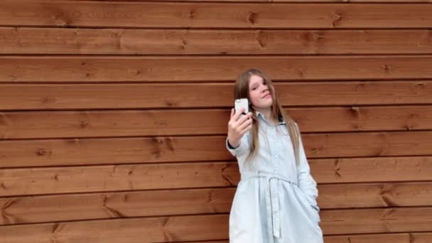 Gelukkig Kaukasische tiener meisje een selfie nemen op haar telefoon houten achtergrond — Stockvideo