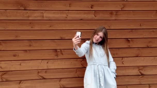 Feliz caucásico adolescente chica tomando un selfie en su teléfono de madera fondo — Vídeos de Stock