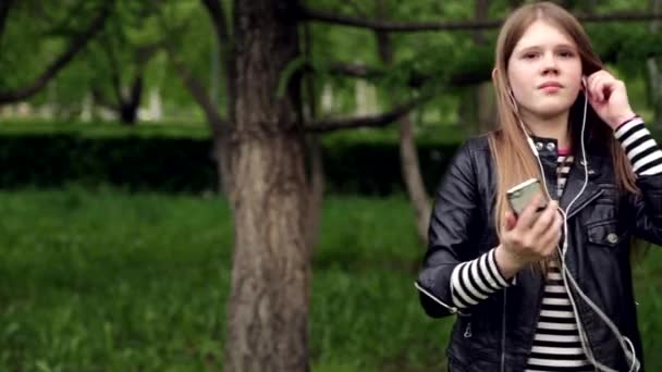 Ganska ung flicka lyssnar musik i hörlurar i parken — Stockvideo