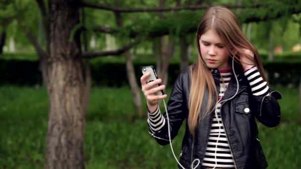 Ganska ung flicka lyssnar musik i hörlurar i parken — Stockvideo