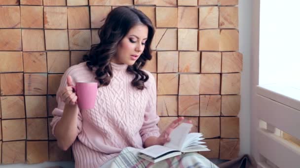 Young woman reading book at home and drinking coffee — Stock Video