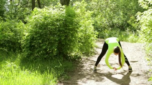 Jonge slanke mooie vrouw doen fitness oefeningen in het park in de buurt van een bos — Stockvideo